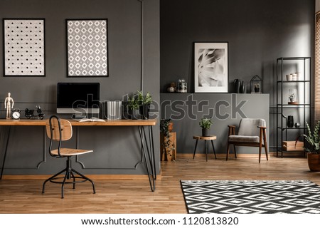 Posters on grey wall above wooden desk with computer monitor in open space interior