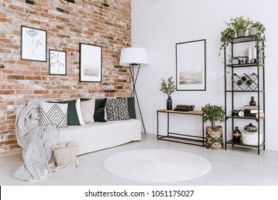 Posters On Red Brick Wall Above White Sofa With Pillows In Bright Living Room Interior With Plants