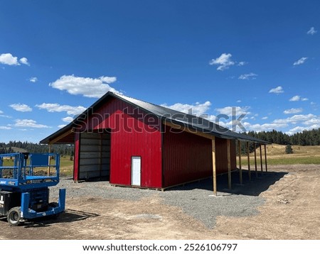 “Finished post-frame building with striking red metal siding. A clean, modern structure showcasing durability and style, perfect for agricultural or commercial use in a beautiful setting.”