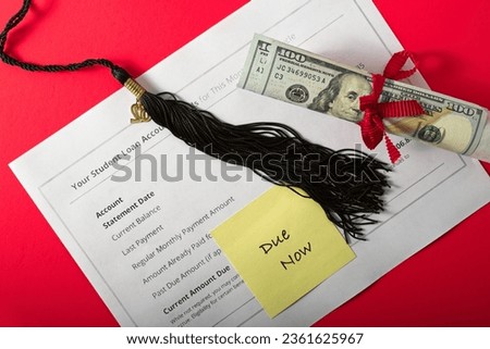 Post-it labeled ‘Due Now’ affixed to student loan invoice under black graduation cap tassel and 100 dollar bill wrapped diploma scroll. Red ribbon and red background. Overhead view