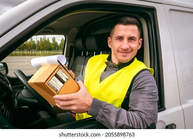 Postman in car. Postman driving van. Mail worker with cardboard box. Deliveryman smiles and looks into camera. Courier service driver. Deliveryman portrait at work. Delivers orders. Postman career
