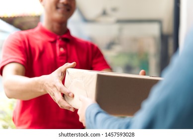 Postman delivering package of goods to home with smile and happy face. Young Asian cute girl receiving boxes from postman at the door. Selective focus on the hands. Home delivery concept.