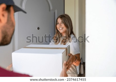 Postman delivers a package to the recipient's home - Young happy woman receives an cardboard order of an online purchase - Customer smiles at the courier - Copy space