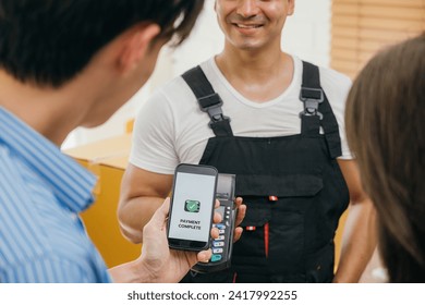 Post-moving couple scans QR code to pay via smartphone. Worker holds a box. Professional movers ensure quality home relocation. Business and industry shown. Online payment for moving