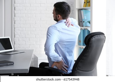 Posture concept. Man suffering from back pain while working with laptop at office