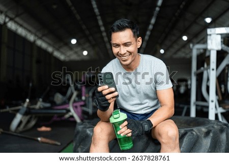 Post-Workout Relaxation. Smiling man checking phone after gym workout, feeling accomplished.