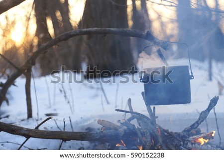 A pot of boiling water on the fire warms in the winter forest