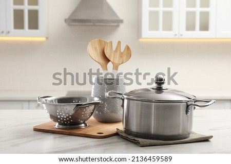Pot, colander and kitchen utensils on white table indoors