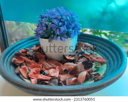 A pot of fake purple flowers in a round plate, surrounded by a sprinkling of crown's god fruit flakes