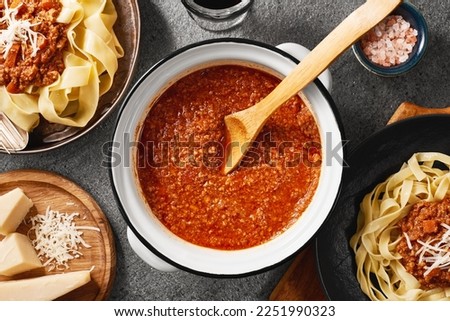 A pot of fresh BOLOGNESE SAUCE and a plats of cooked pappardelle and tagliatelle pasta with bolognese sauce. Gray background from natural stone. Top view.