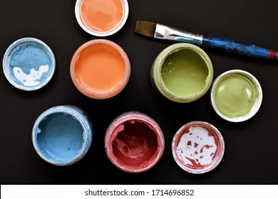 A Pot Full Of Strong Paint Lies On A Dark Surface, On Top Of It Lies A Brush - Concept For Art, Focus On The Paint Pots And The View From Above