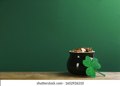 Pot Of Gold Coins And Clover On Wooden Table Against Green Background, Space For Text. St. Patrick's Day Celebration