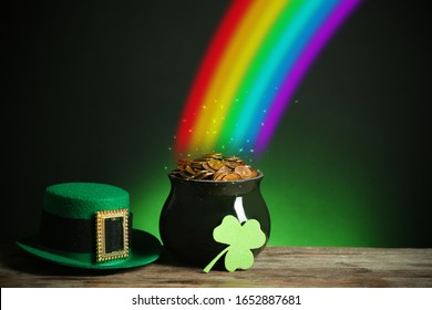 Pot with gold coins, hat and clover on wooden table against dark background, space for text. St. Patrick's Day