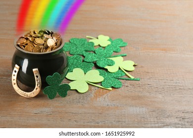 Pot with gold coins, horseshoe and clover leaves on wooden table. St. Patrick's Day celebration
