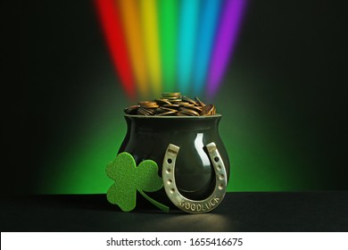 Pot with gold coins, horseshoe and clover on table against dark background. St. Patrick's Day