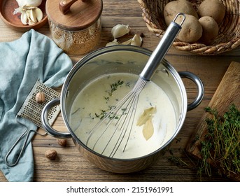 Pot With Milk Cream And Herbs For Making Potato Gratin On Rustic Wooden Kitchen Table, Top View