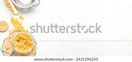Pot with raw conchiglie pasta on light wooden background with space for text