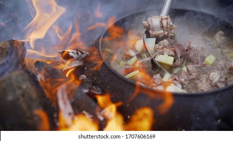 A pot of soup cooked over a fire. Stir soup with soup ladle, which is cooked in a cast iron over a fire. food in a big kettle cooked on fire