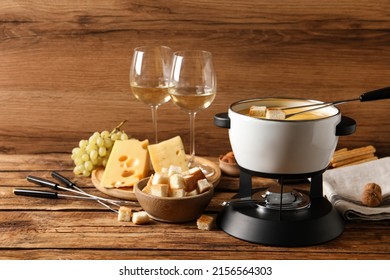 Pot Of Tasty Cheese Fondue, Snacks And Wine On Wooden Table