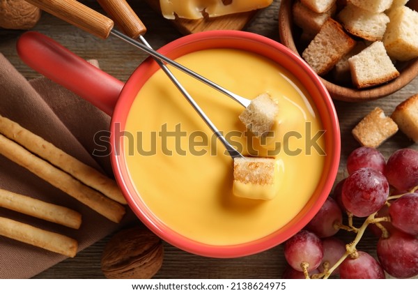 Pot of tasty cheese fondue and snacks on wooden\
table, flat lay