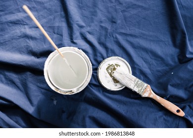 Pot Of White Paint With Brush On Top Of Blue Drop Sheet Ready To Paint, Shot At Shallow Depth Of Field With Paint Can Text Blurred