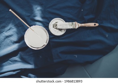 Pot Of White Paint With Brush On Top Of Blue Drop Sheet Ready To Paint, Shot At Shallow Depth Of Field With Paint Can Text Blurred