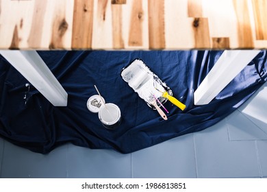 Pot Of White Paint With Paint Tray Roller And Brushes On Top Of Blue Drop Sheet Ready To Paint A Table, Shot At Shallow Depth Of Field With Paint Can Text Blurred