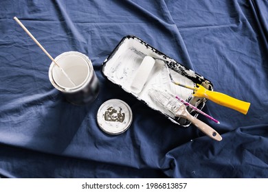 Pot Of White Paint With Paint Tray Roller And Brushes On Top Of Blue Drop Sheet Ready To Paint, Shot At Shallow Depth Of Field With Paint Can Text Blurred