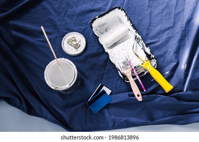 Pot Of White Paint With Paint Tray Roller And Brushes With Payment Card On Top Of Blue Drop Sheet Concept Of Costs Of DIY And Renovating, Shot At Shallow Depth Of Field With Paint Can Text Blurred