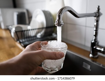 Potable Water And Safe To Drink. Man Filling A Glass Of Water From A Stainless Steel Kitchen Tap. Male's Hand Pouring Water Into The Glass From Chrome Faucet To Drink Running Water With Air Bubbles.