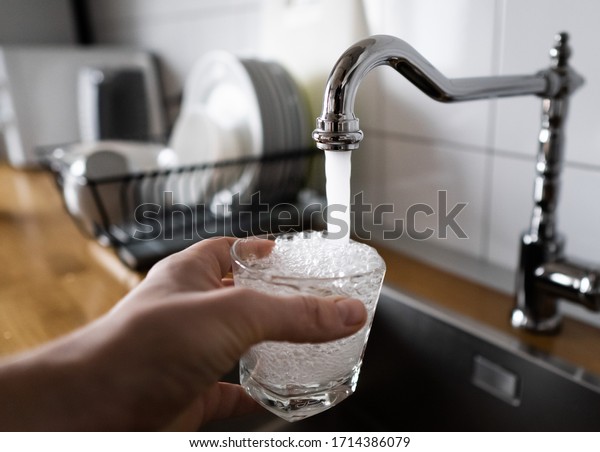 potable water and safe to drink. man filling a\
glass of water from a stainless steel kitchen tap. male\'s hand\
pouring water into the glass from chrome faucet to drink running\
water with air bubbles.