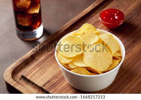 Potato chips in a bowl with dip sauce on wooden service tray and glass of coke. Close up view