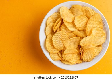Potato chips in bowl on yellow background, top view. Unhealthy food, rich in saturated fatty acids