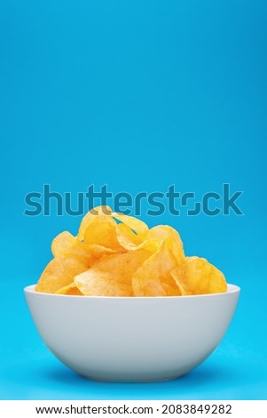 Potato chips or crisps in white bowl on blue background