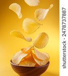 Potato chips falling into a wooden bowl isolated on yellow background, food blog, snacks