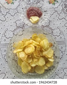 potato chips in glass dish next to red sauce in glass pyrex on white background.