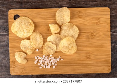 Potato chips on a wooden board with coarse salt are good for beer or ale snacks on a wooden table. - Powered by Shutterstock