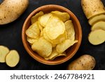 Potato chips in a wooden plate and raw potatoes close-up, background. Top view