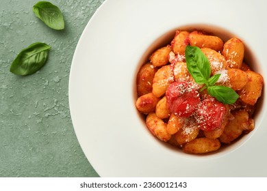 Potato gnocchi. Traditional homemade potato gnocchi with tomato sauce, basil and parmesan cheese on kitchen table on light green kitchen table background. Traditional Italian food. Top view.