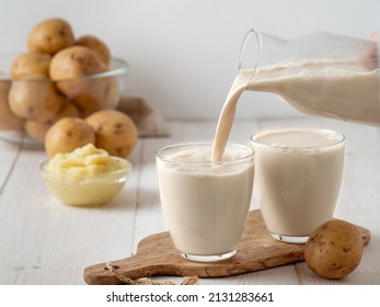 Potato milk pouring into glass on white wooden background. Pouring vegan milk in glass, with potato puree and potato tubers on background. Copy space. Home made potato milk made from boiled potatoes - Shutterstock ID 2131283661