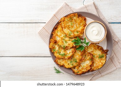 Kartoffelpfannkuchen oder Latzen oder Darikati mit sauer Sahne in Teller auf weißem Holztisch. Draufsicht. Kopiert Platz.