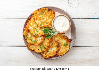 Potato pancakes or latkes or draniki with sour cream in plate on white wooden table. Top view. Copy space.