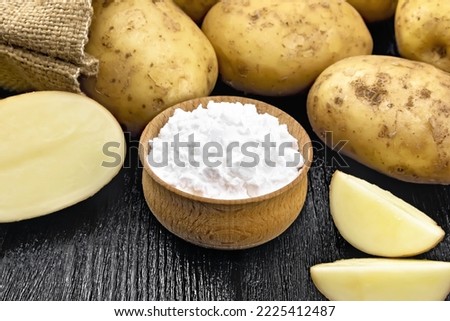 Potato starch in bowl, vegetable tubers in a bag and on a table against the background of wooden board