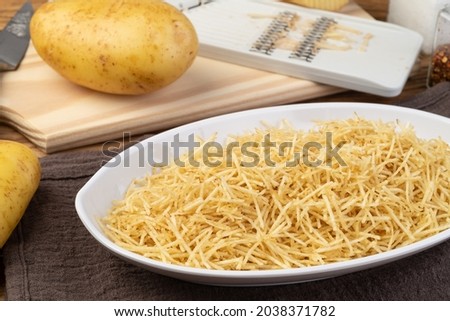 Potato straw or shoestring potato in a white plate with raw potatoes.