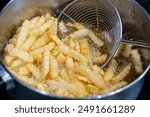 Potatoes in boiling oil, homemade french fries, deep fried potato cooking in metal fryer pot, fat fast food cooking, oily bubbles texture closeup