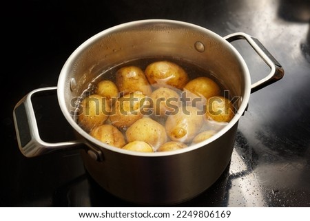 Potatoes with peel in a stainless steel pot with boiling water on the stove, healthy cooking concept, copy space, selected focus, narrow depth of field