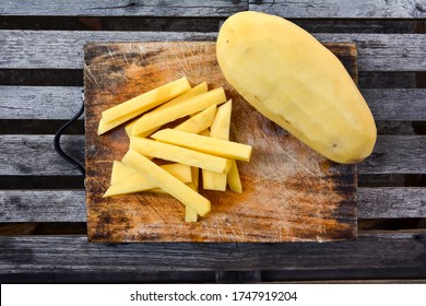 Potatoes sliced sticks for french fries on chopping board and wood table background. Fresh potato pieces cut bar on cutting board with peel