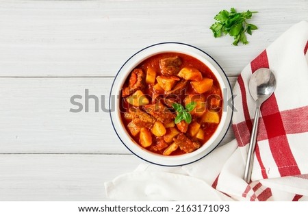 Potatoes stewed with meat, in tomato sauce, with spices and herbs, no people, on a white table,
