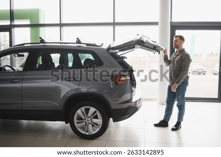 Potential customer inspecting trunk space of a new suv crossover in a modern car dealership showroom