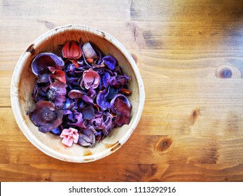Potpourri of violet, purple and pink flowers and barks inside bamboo bowl on rustic wooden table.